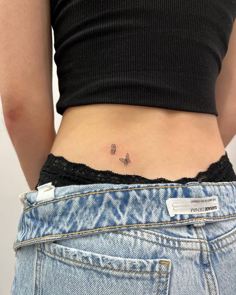 Fine line style little butterfly couple tattoo located on the lower back.