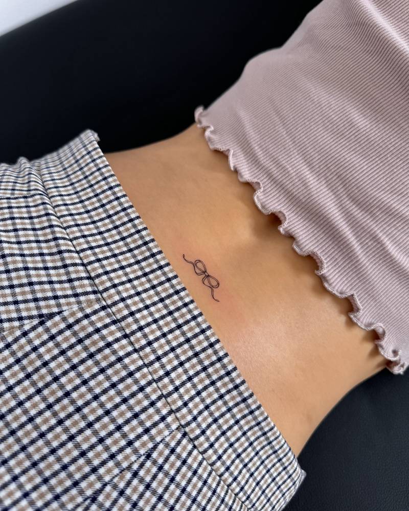 Bow tattoo in fine line style located on the lower back.