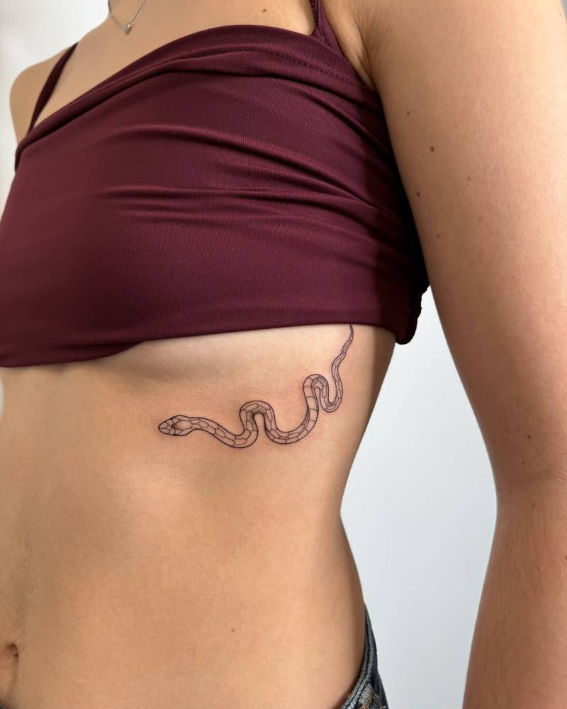 Snake tattoo in fine line style placed on the under boob.