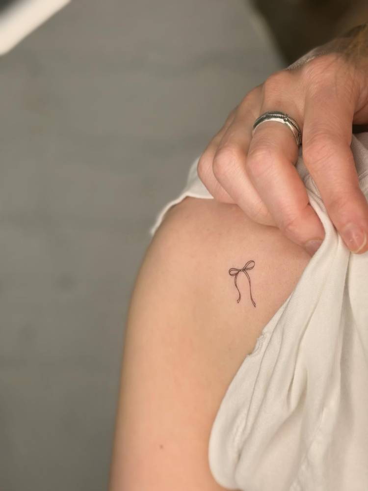 Bow tattoo located on the shoulder, done in fine line style.