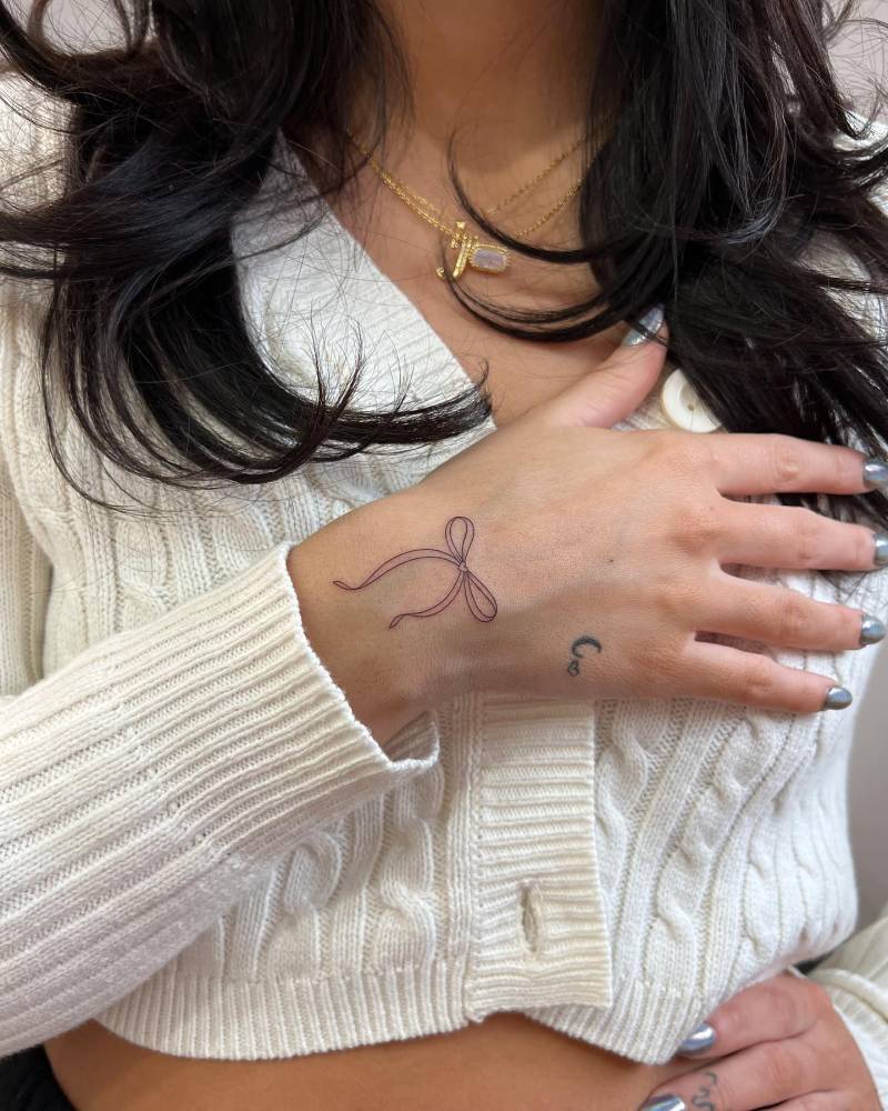 Fine line style bow tattoo located on the wrist.