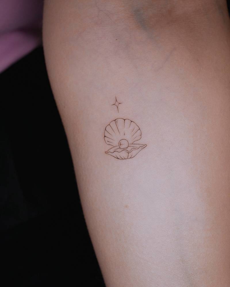 Scallop tattoo located on the inner forearm, done in fine line style.
