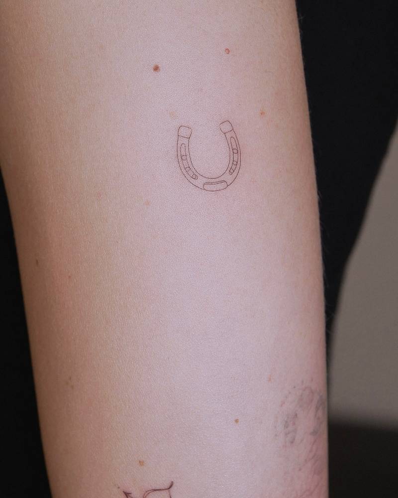 Horseshoe tattoo in fine line style placed on the upper arm.