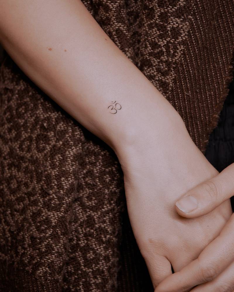 Tiny minimalistic Om tattoo located on the wrist.