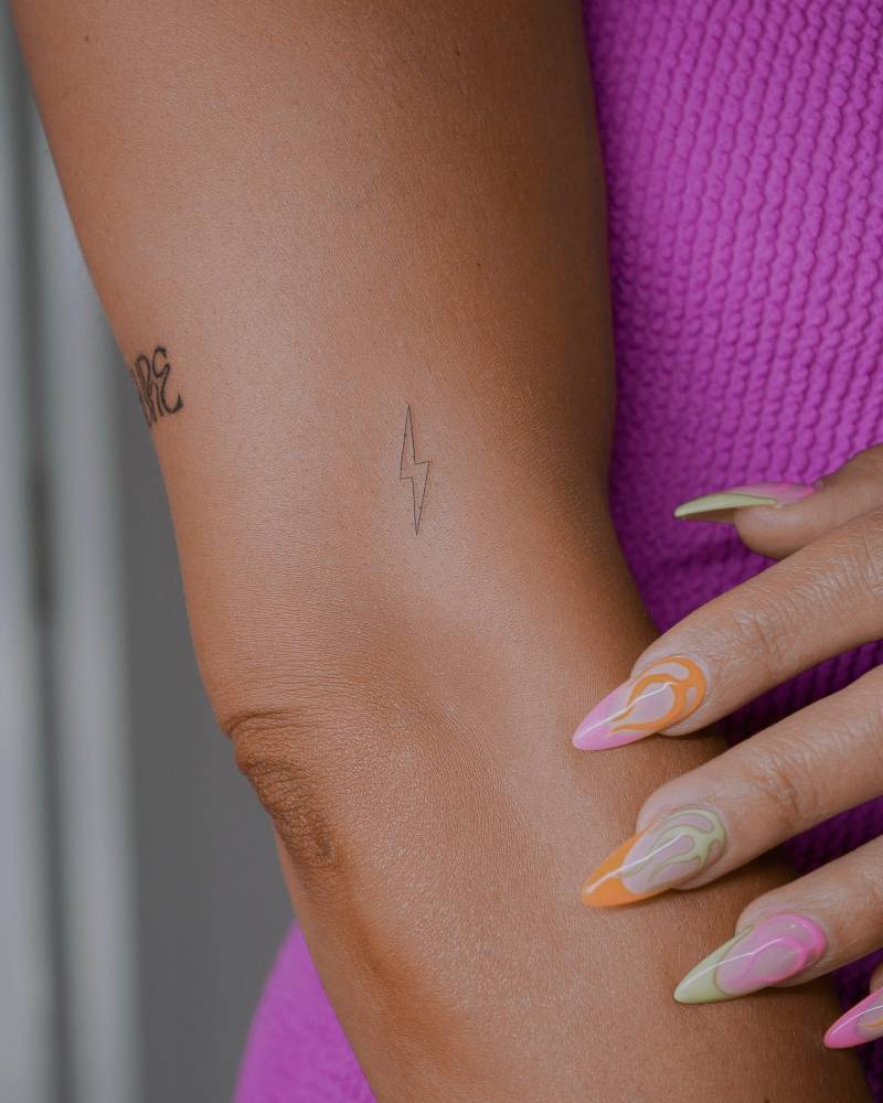 Minimalistic lightning bolt tattoo in fine line style located on the upper arm.