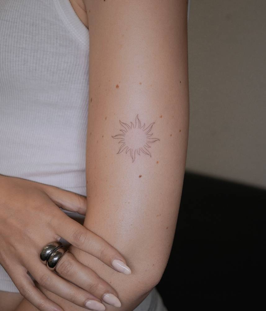 Sun tattoo in fine line style placed on the upper arm.