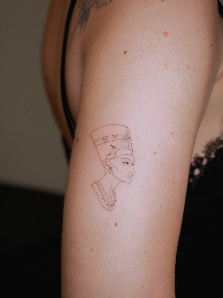 Nefertiti portrait tattoo in fine line style done on the upper arm.