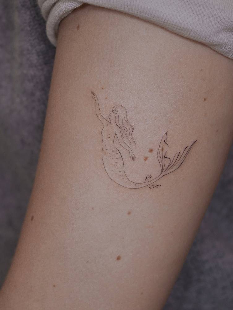 Mermaid tattoo in fine line style located on the upper arm.