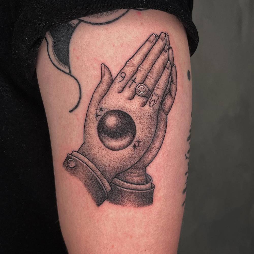 Praying hands tattoo in dotwork style located on the upper arm.