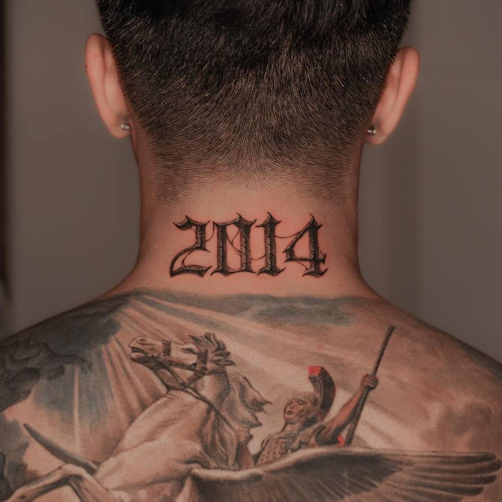 Year "2014" lettering tattoo in gothic font located on the back of the neck.