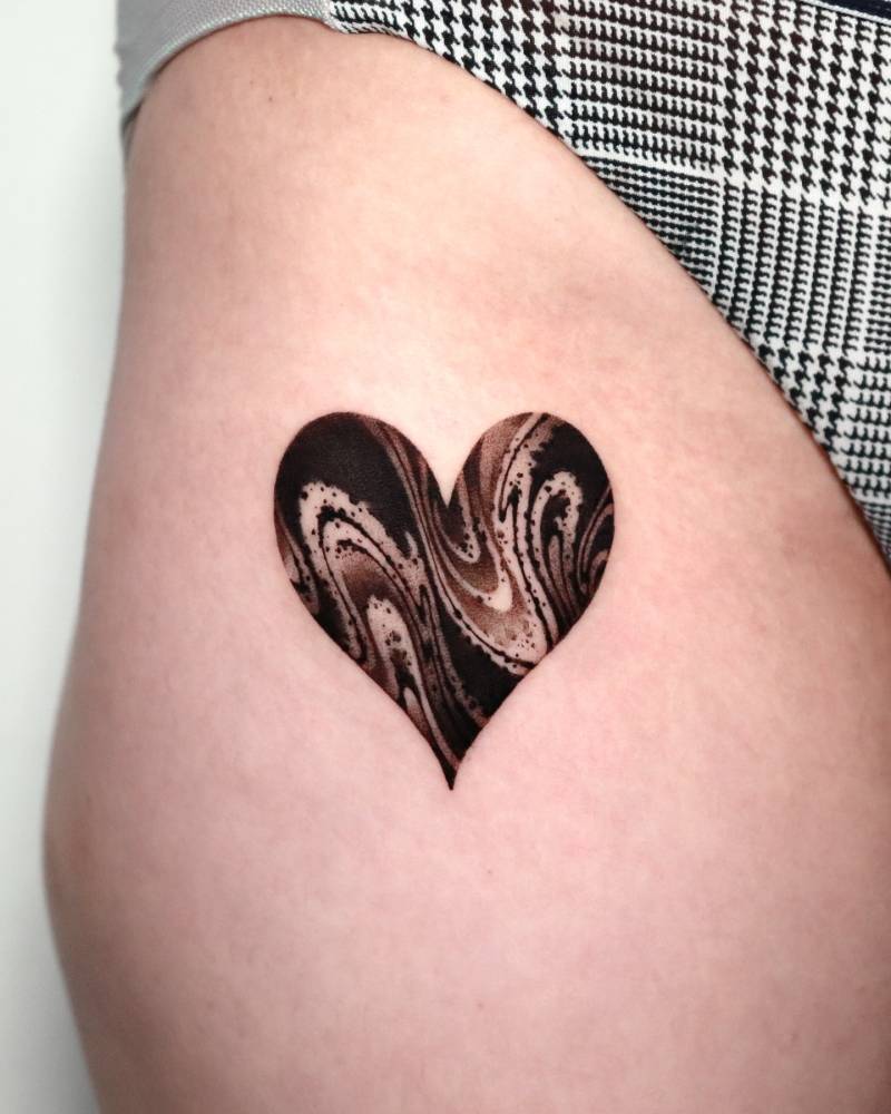 Abstract heart tattoo located on the pelvis, done in blackwork style.