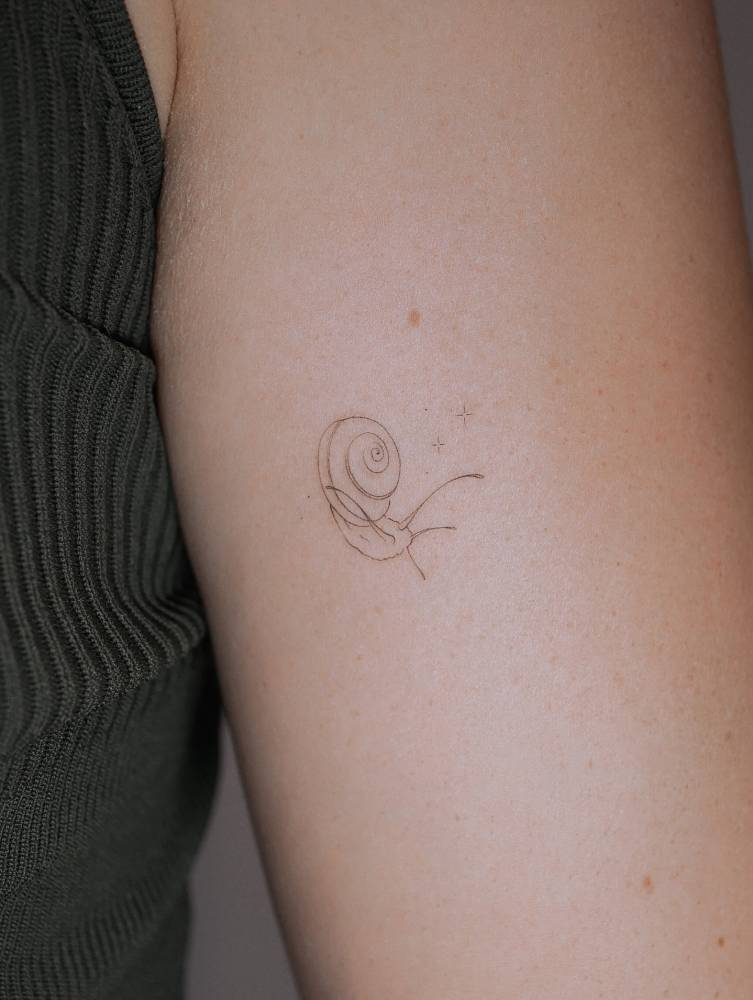 Fine line style snail tattoo located on the tricep.
