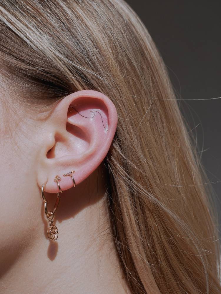 Wave tattoo in minimalistic style located on the ear.