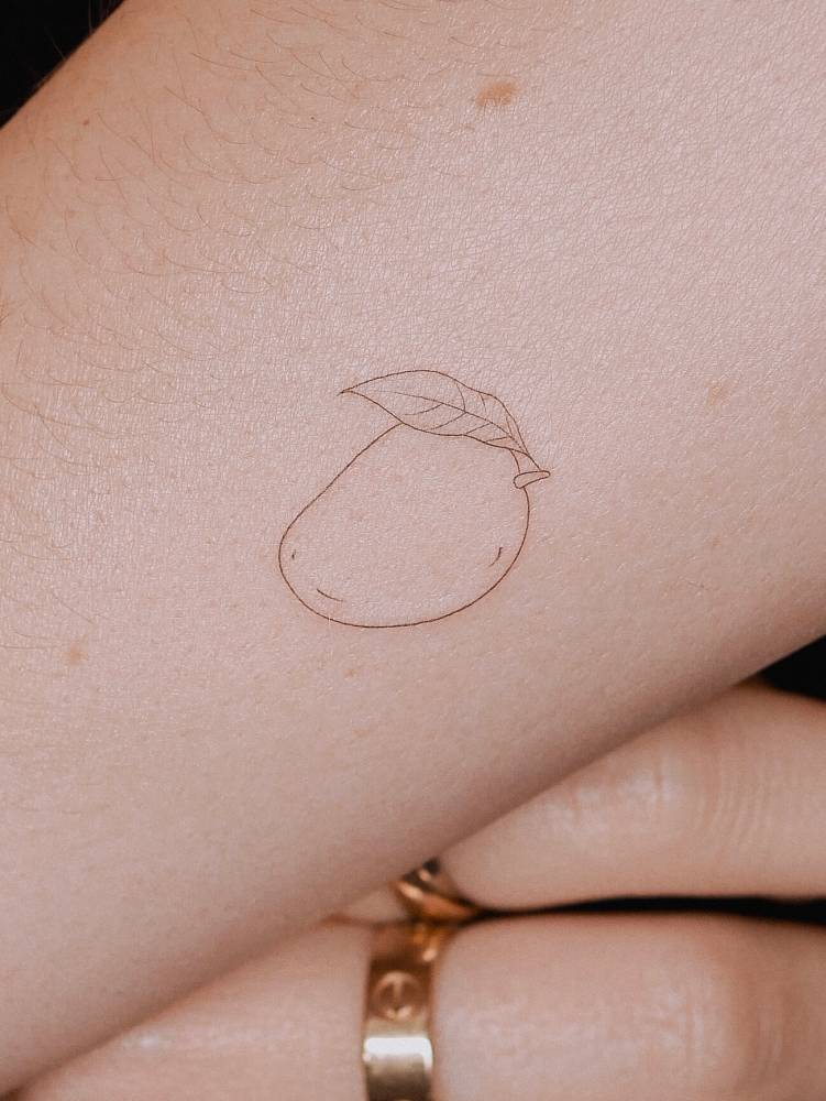 Tiny minimalistic mango in fine line style tattooed on the forearm.