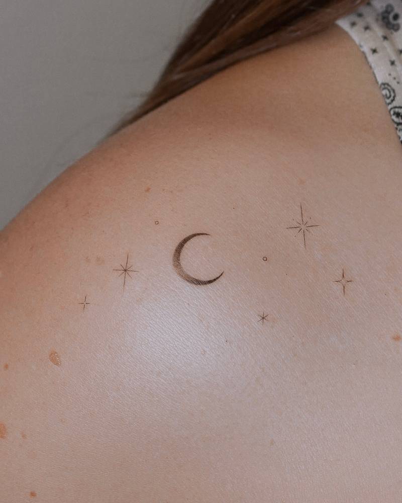 Crescent moon and sparkling stars tattoo located on the shoulder.