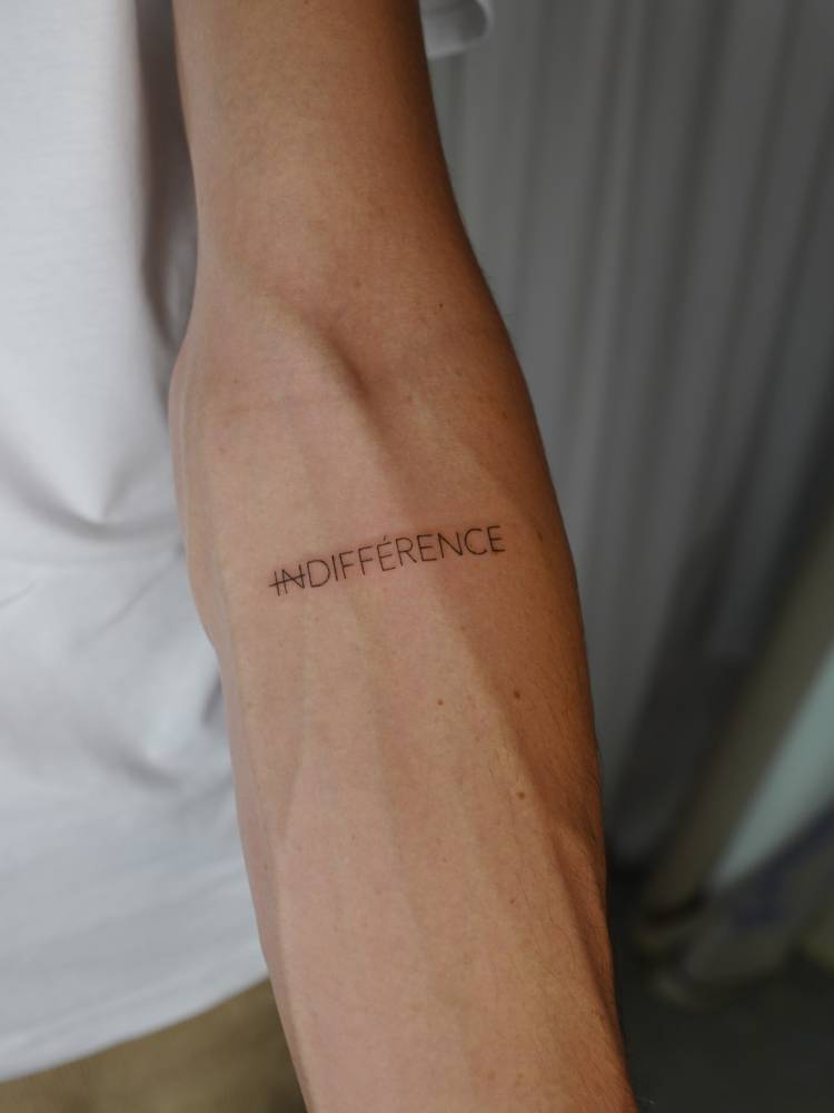 "Indifference" lettering tattoo in handwritten font located on the inner forearm.