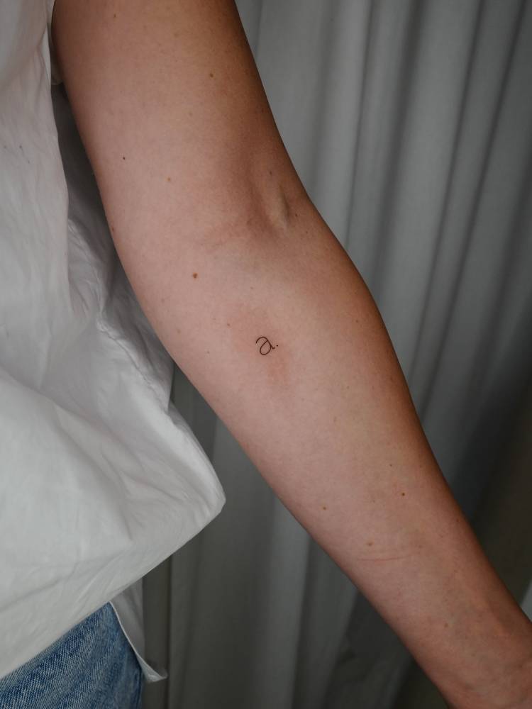 Tiny letter "A" tattoo in typewriter font located on the inner forearm.