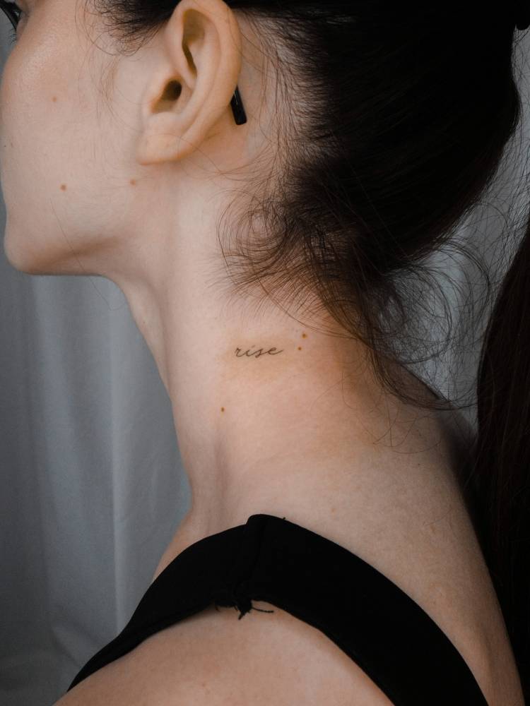Handwritten font word "rise" tattooed on the neck.