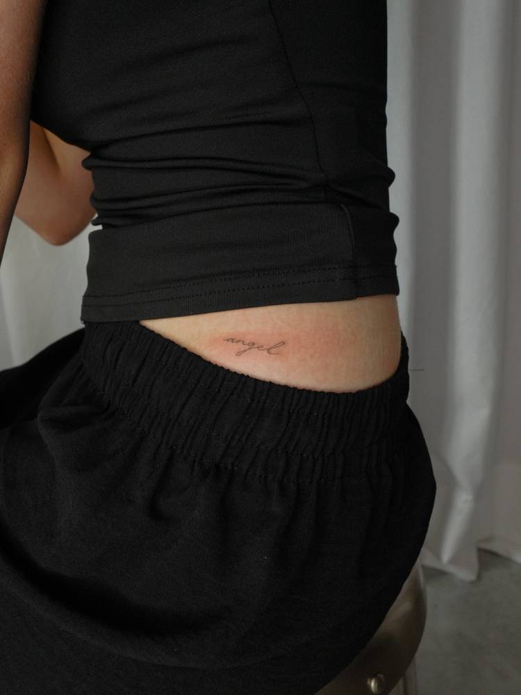 Lettering tattoo of the word "angel" placed on the hip.