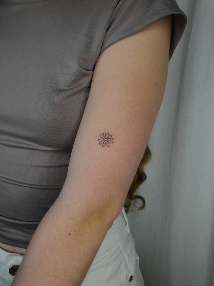 Minimalistic style daisy flower tattoo placed on the upper arm.
