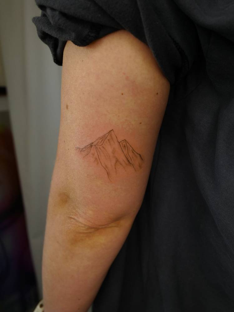 Illustrative style mountains tattoo placed on the tricep.