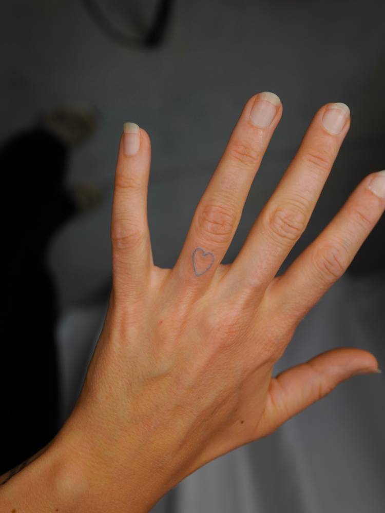 Tiny minimalistic blue heart tattoo located on the finger.