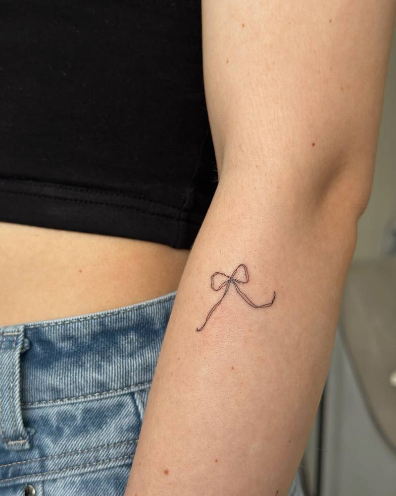 Fine line style bow tattoo located on the forearm.