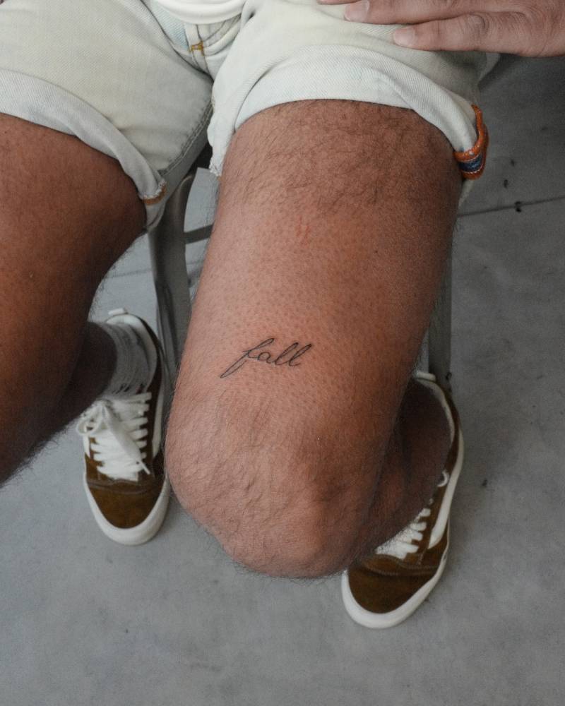 Handwritten word "fall" tattooed on the thigh.