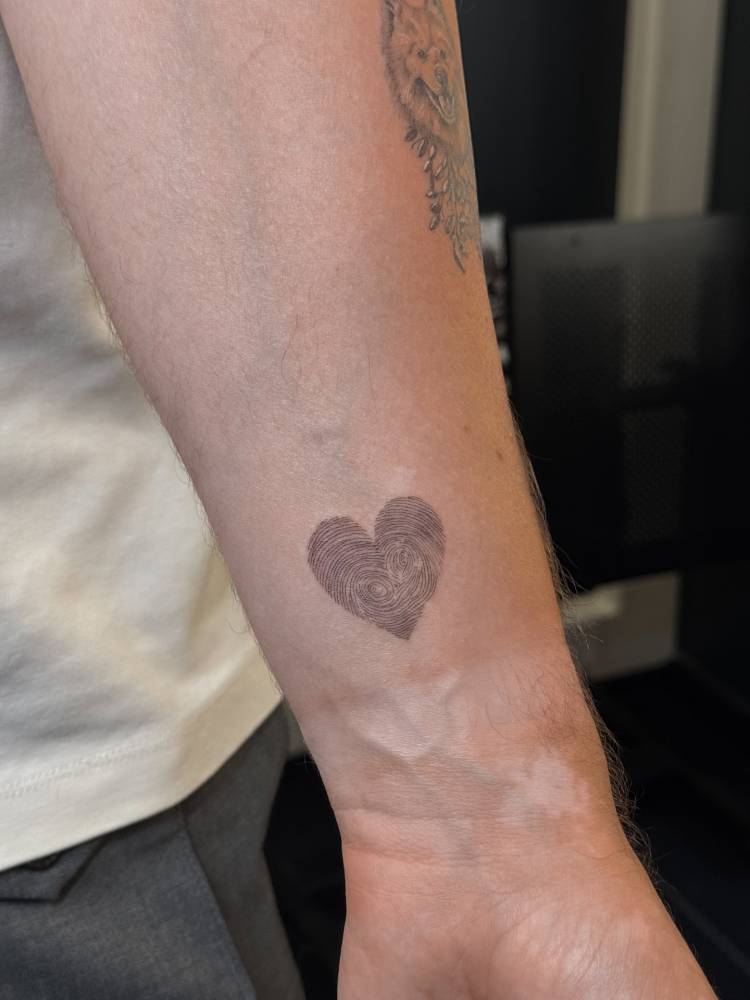 Fingerprint heart tattoo located on the wrist, done in fine line style.