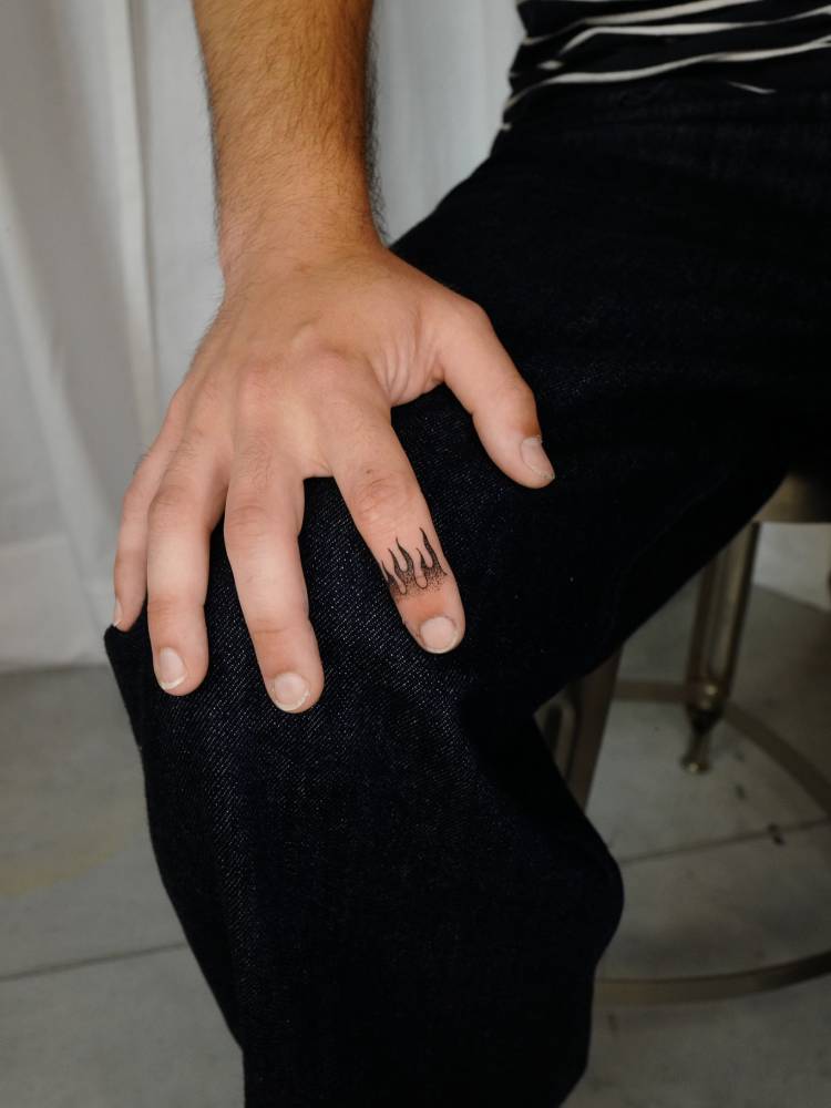 Tiny fire tattoo located on the finger, illustrative style.