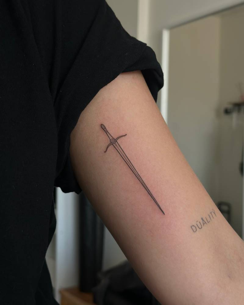 Little sword tattoo in illustrative style done on the inner arm.