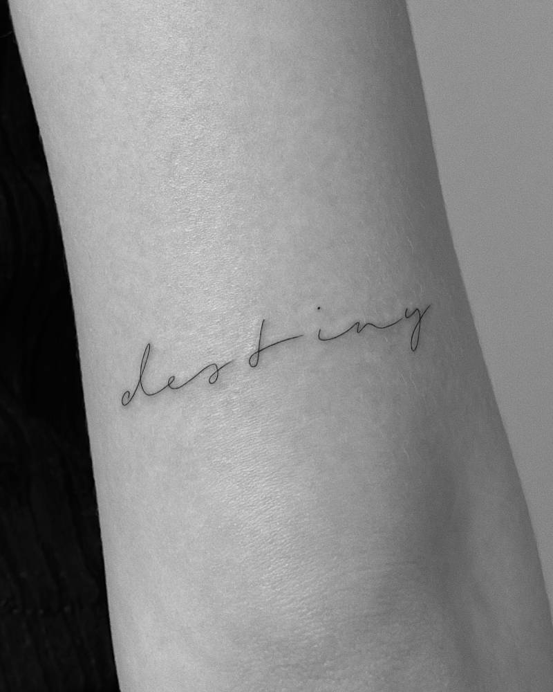 Lettering tattoo of the word "destiny" handwritten on the tricep.