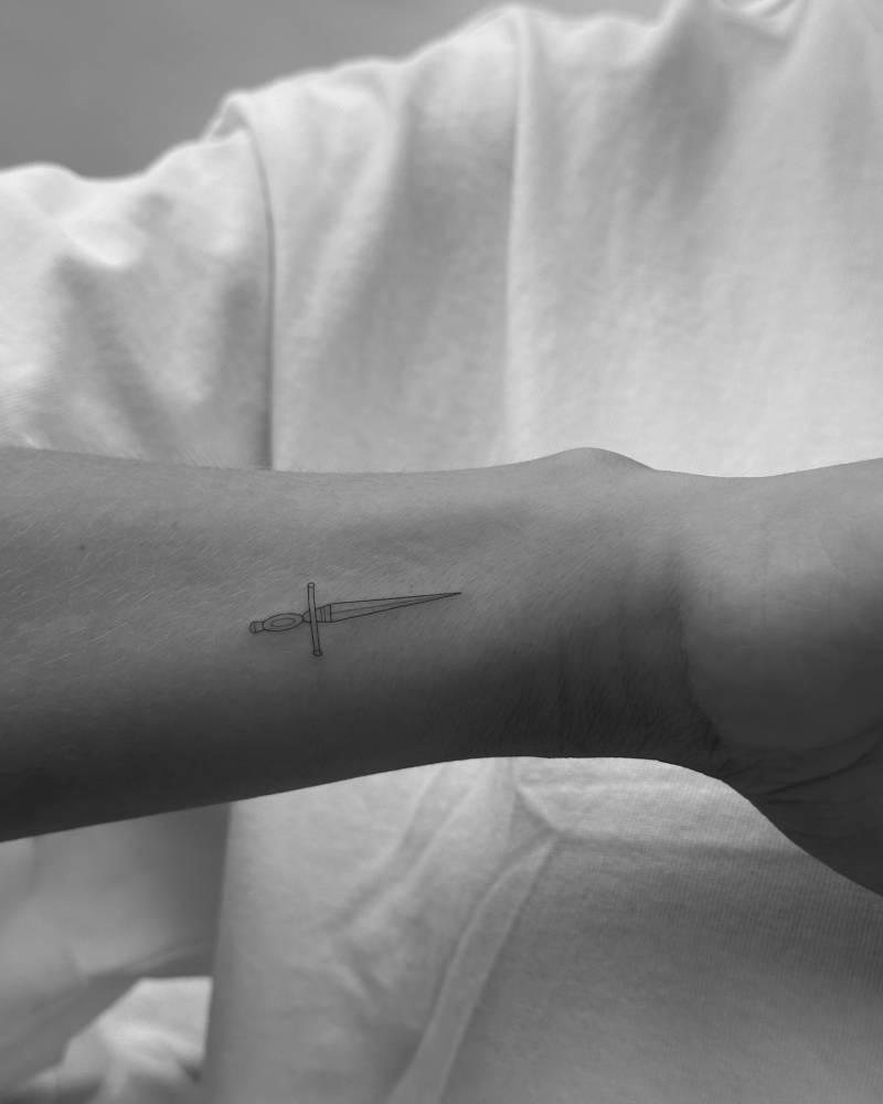 Little dagger tattoo in fine line style located on the wrist.