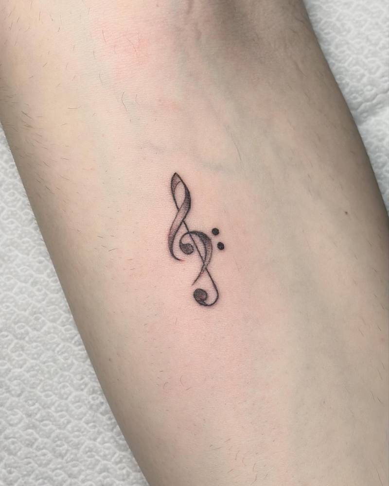 Treble clef tattoo located on the inner forearm, done in illustrative style.