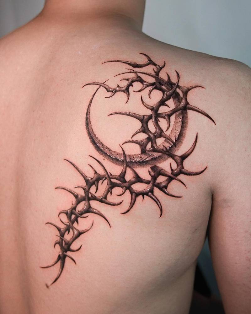 Thorns and crescent moon tattoo located on the shoulder blade.