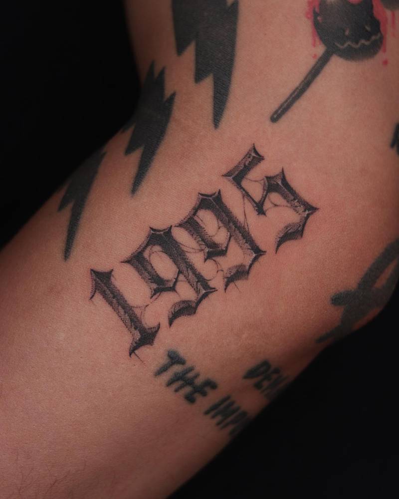 Gothic font "1995" lettering tattoo located on the forearm.