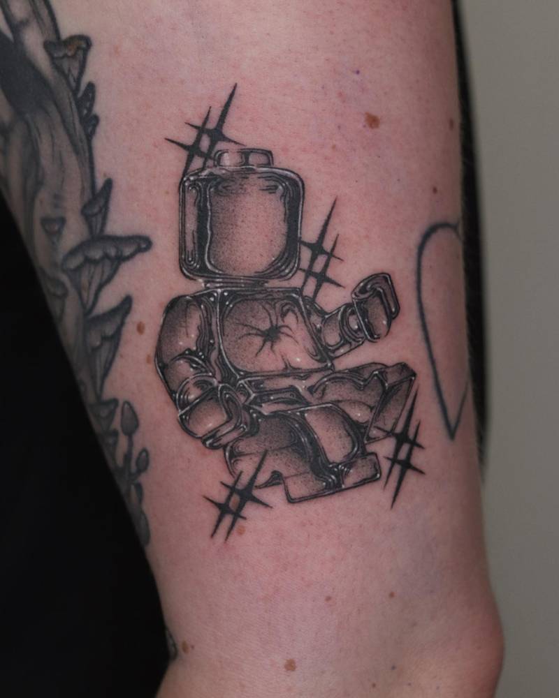 Metallic effect lego minifigure tattoo located on the upper arm.