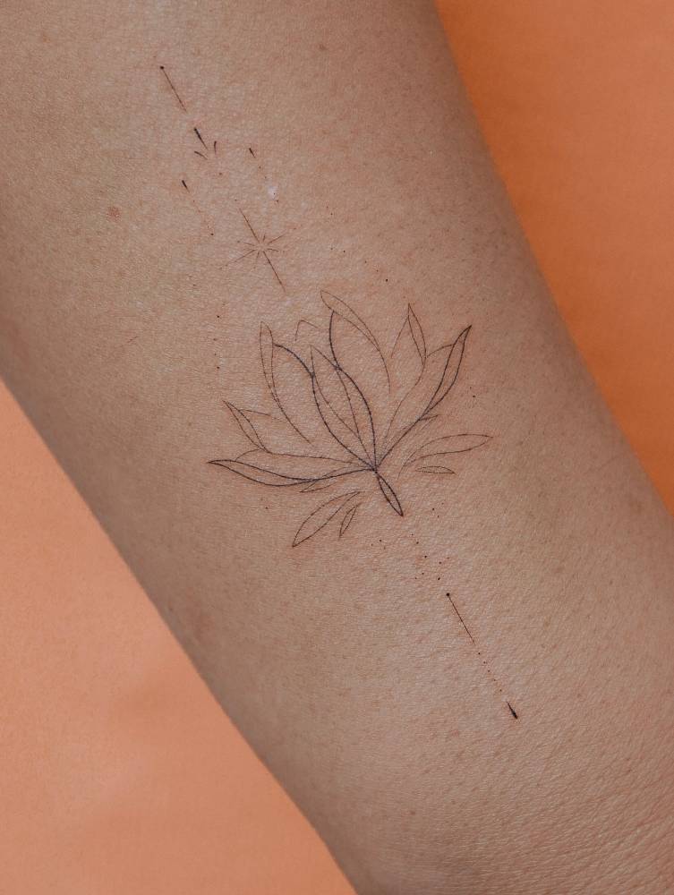 Ornamental lotus flower tattoo located on the forearm, done in fine line style.