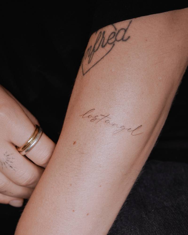 "Lost angel" lettering tattoo located on the forearm.