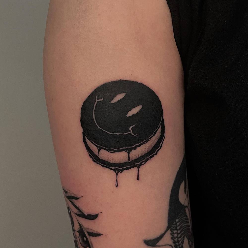 Smiley macaron tattoo located on the upper arm.