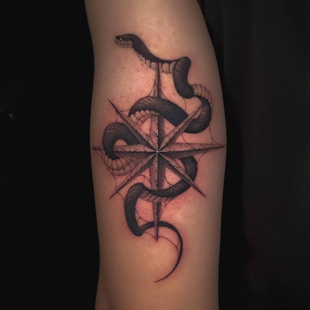 Compass rose and snake tattoo in illustrative style located on the tricep.