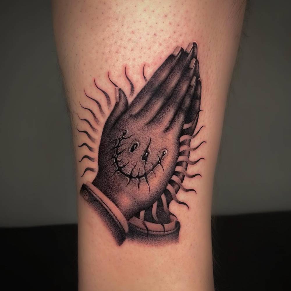 Smiley praying hands tattoo located on the shin.