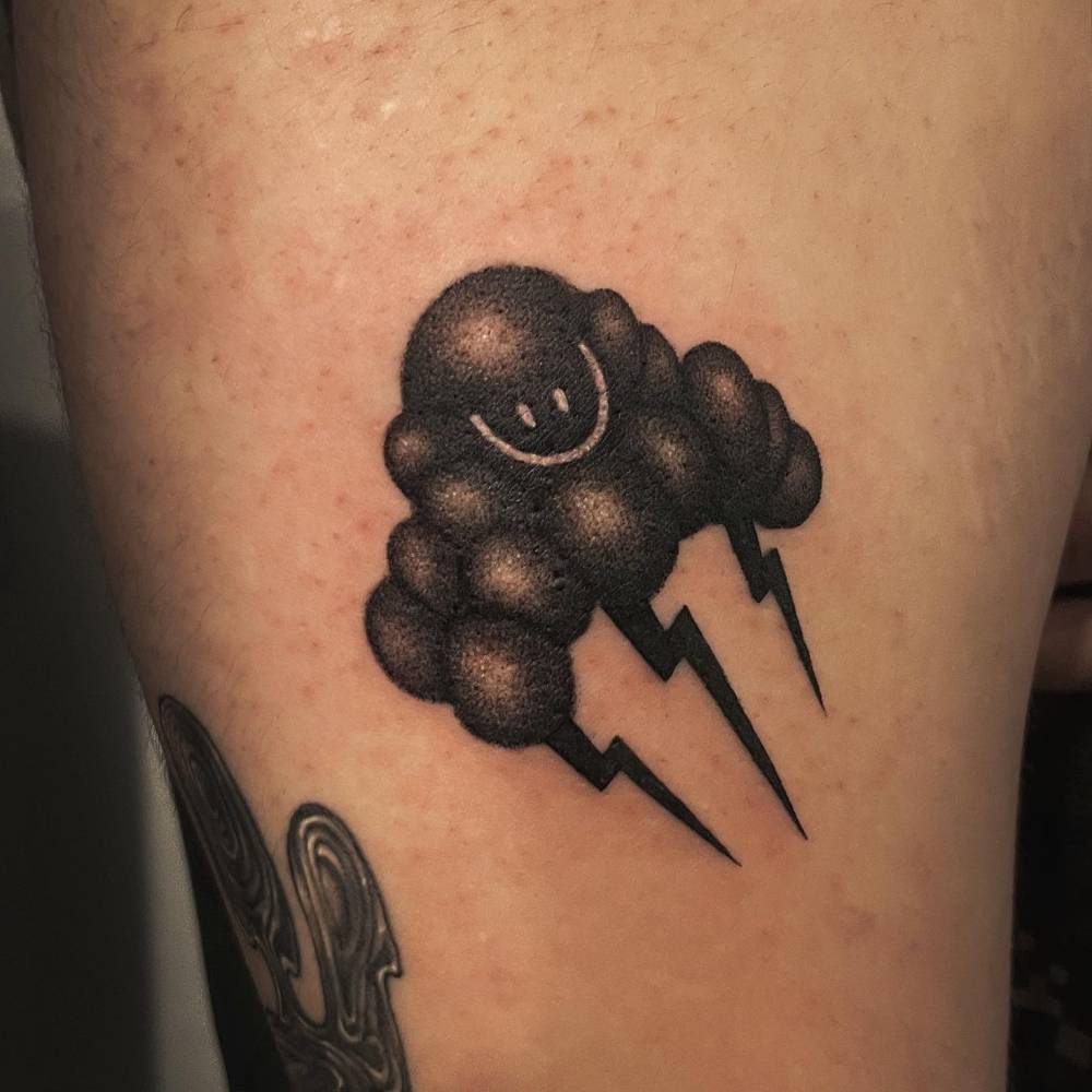Smiley cloud tattoo in blackwork style located on the thigh.