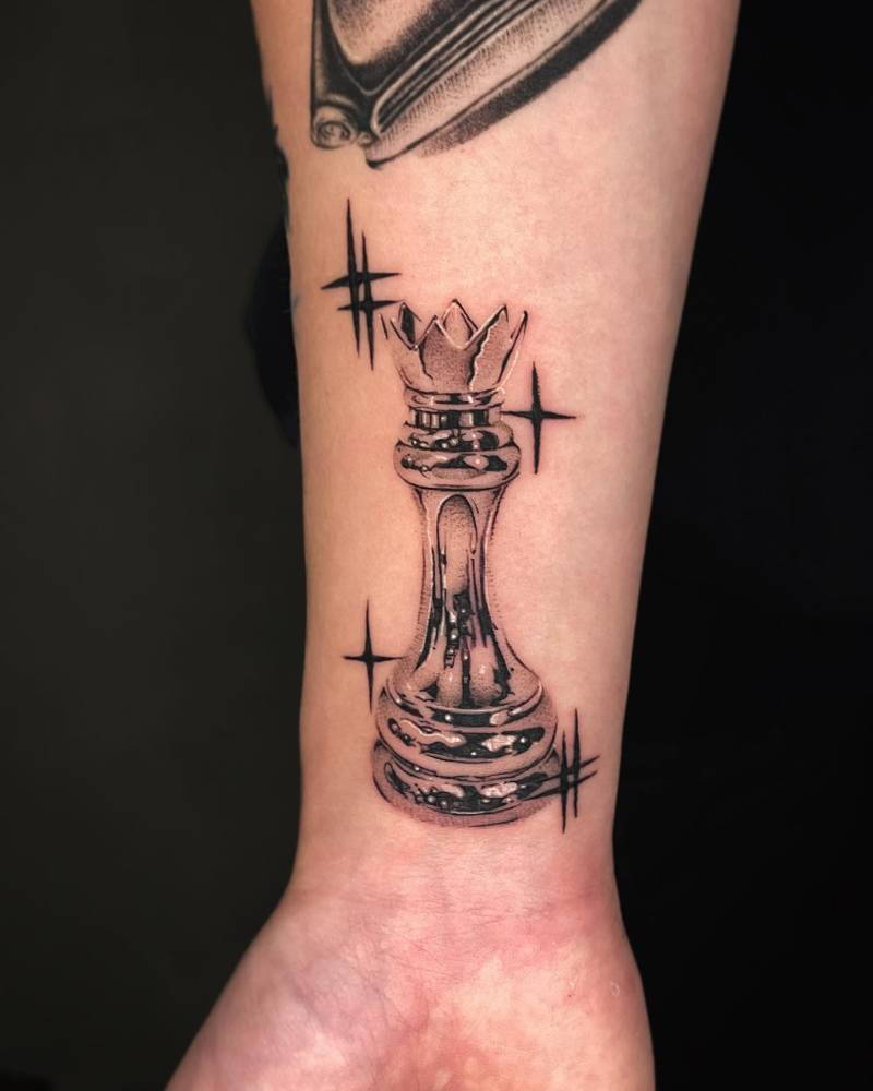 Metallic effect chess king tattoo located on the wrist.