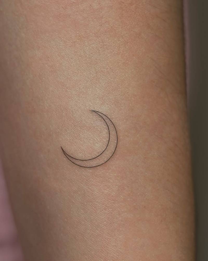 Fine line style crescent moon tattoo located on the upper arm.