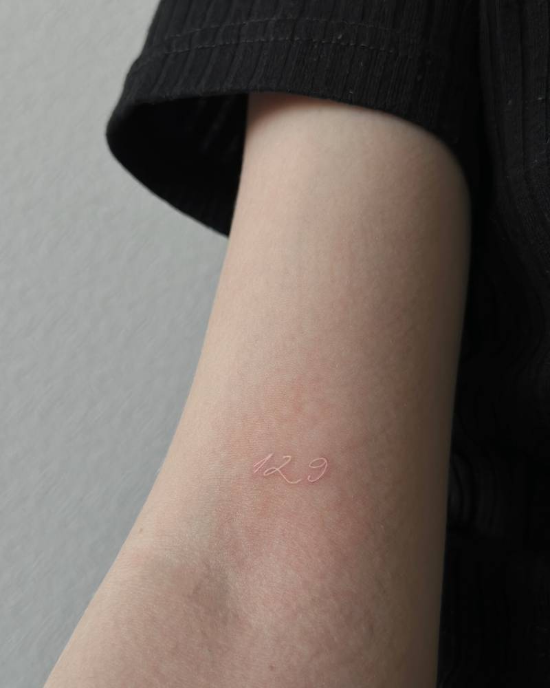 Tattoo of the number "129" in white ink located on the bicep.