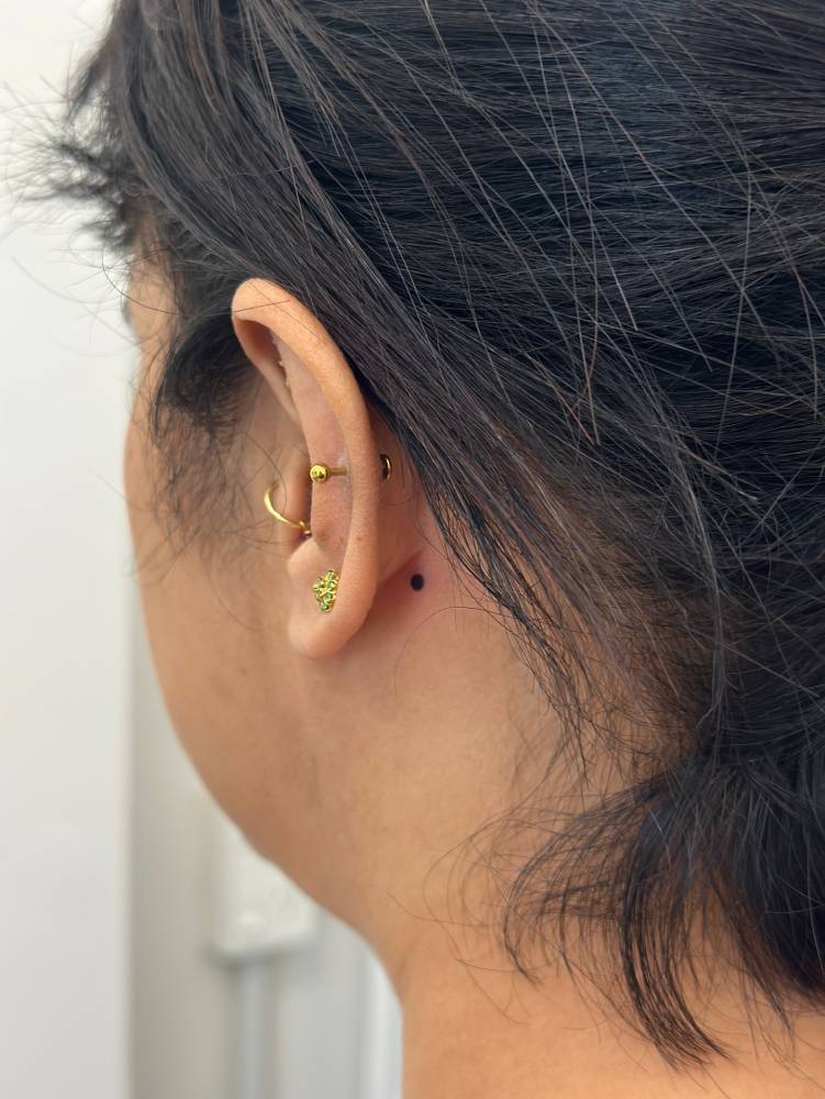 Tiny minimalistic dot tattooed behind the ear.