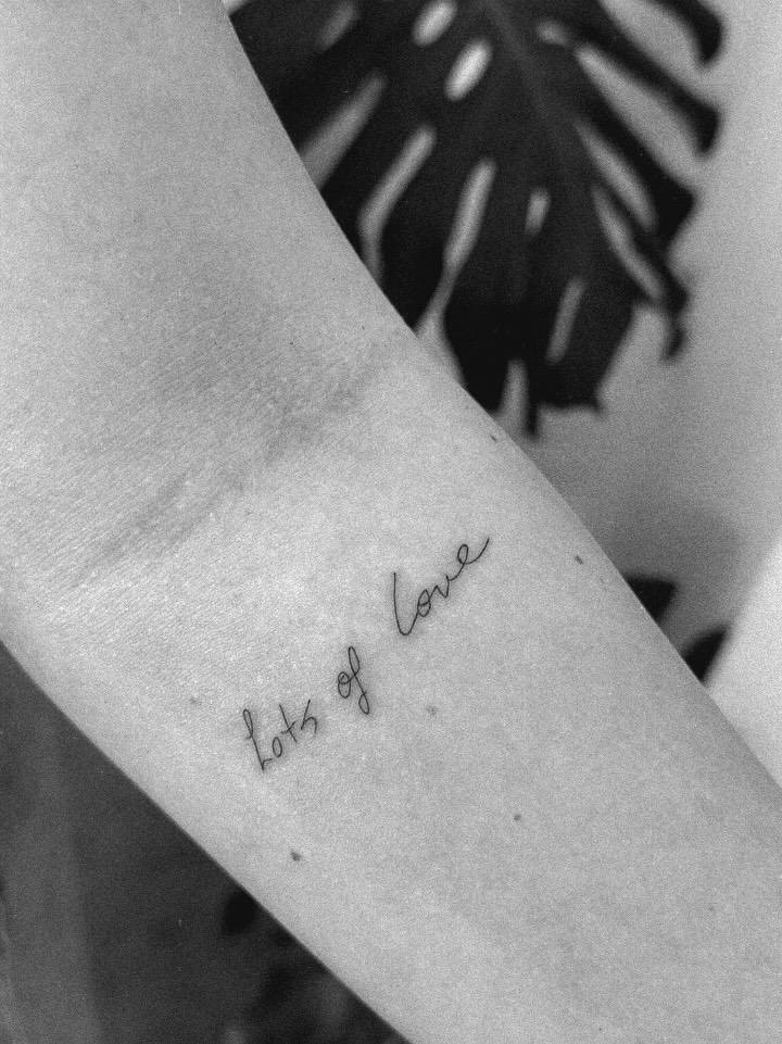 Handwritten lettering tattoo that says "lots of love" located on the inner forearm.