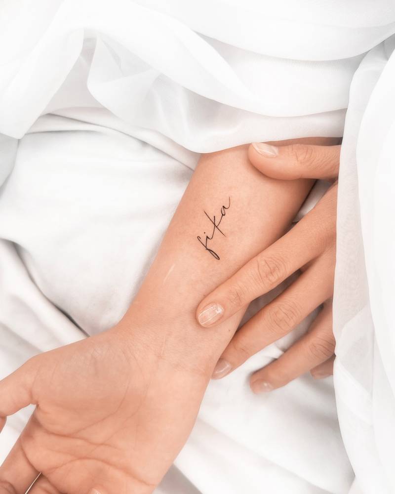 Lettering tattoo of the word "fika" located on the wrist.