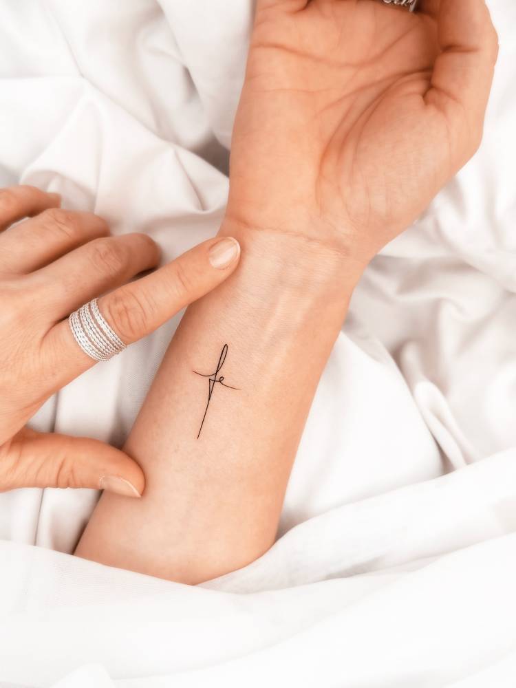 "Fe" cross lettering tattoo in handwritten font located on the wrist.